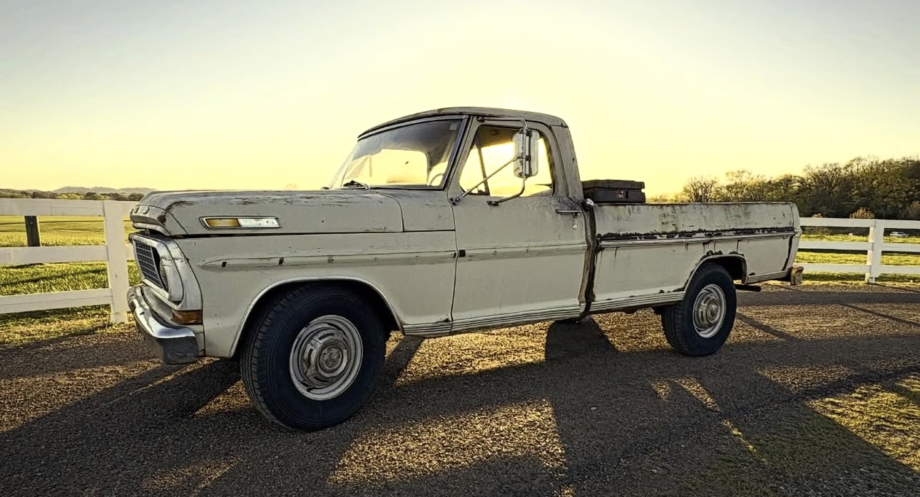 A restored cream 1970 Ford F-250 parked beside a white fence in the Tennessee countryside at golden hour
